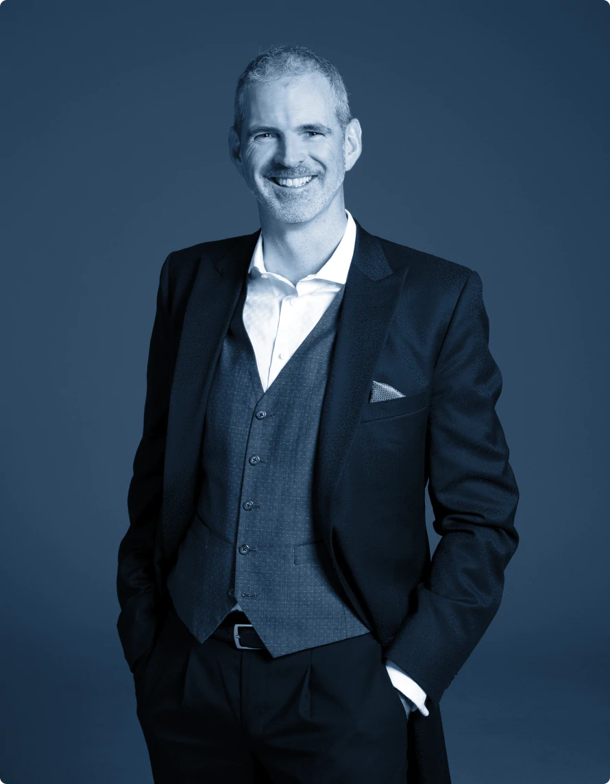 Dave Higgins, smiling in a three-piece suit with an open-necked shirt, looking casual and relaxed with his hands in his pockets